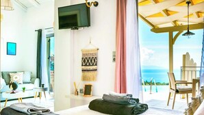 A hotel room with a bed, a TV, a view of the ocean, and a balcony with a chair. - Villa Baby Lemoni (Kefalonia)