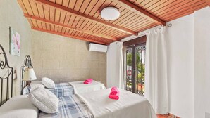 A room with two beds, a ceiling fan, a window with curtains, and a wall-mounted air conditioner.