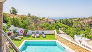 A pool area with a view of the sea, surrounded by greenery and a stone wall.