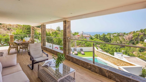 A spacious balcony with a pool, outdoor furniture, and a scenic view of hills and the sea.