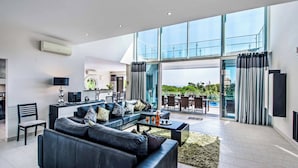A modern living room with a black leather sofa, a dining area, and a large glass door leading to an outdoor terrace.