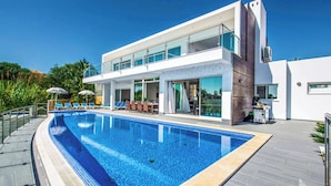 A modern two-story building with a swimming pool, outdoor seating, and a clear blue sky.