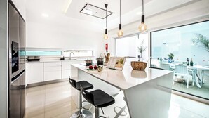 A modern kitchen with a central island, bar stools, pendant lighting, and a large window offering a view of the outdoors. - Villa Aventura (Albufeira)