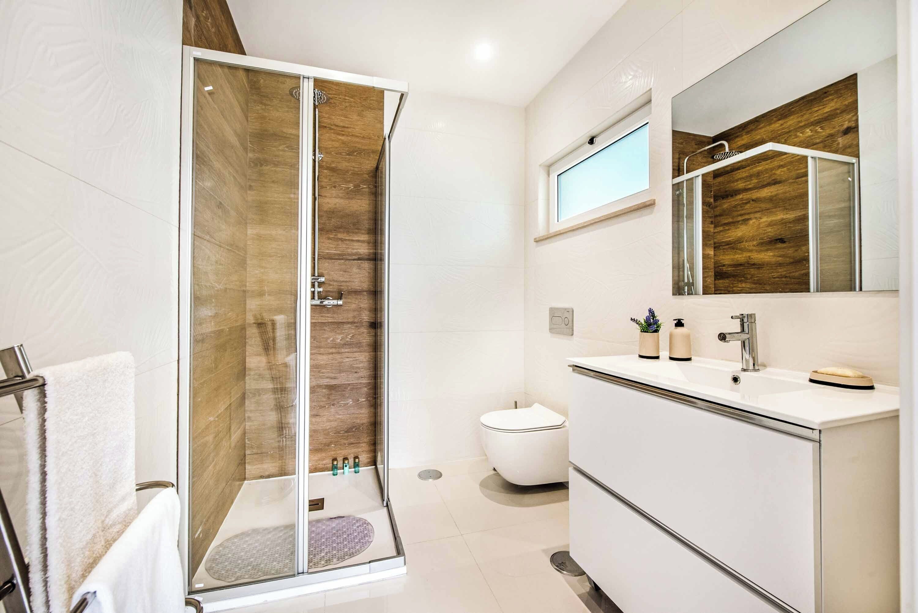 Une salle de bain moderne avec une douche à parois de verre, des toilettes blanches et un meuble-lavabo avec un miroir.