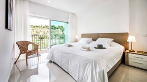 A hotel room with a large bed, a chair, a nightstand, and a view of greenery outside. - Villa Aventura (Albufeira)