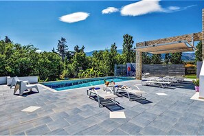 A poolside area with lounge chairs, a small table with a vase, and a pergola providing shade.