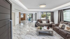 A modern living room with a marble floor, two sofas, a coffee table, and a dining area in the background. - Villa Christina Coral (Pegeia)