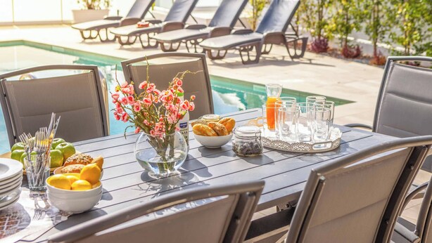 A poolside dining area with a table set for breakfast, including fruits, pastries, and beverages. - Villa Christina Coral (Pegeia)