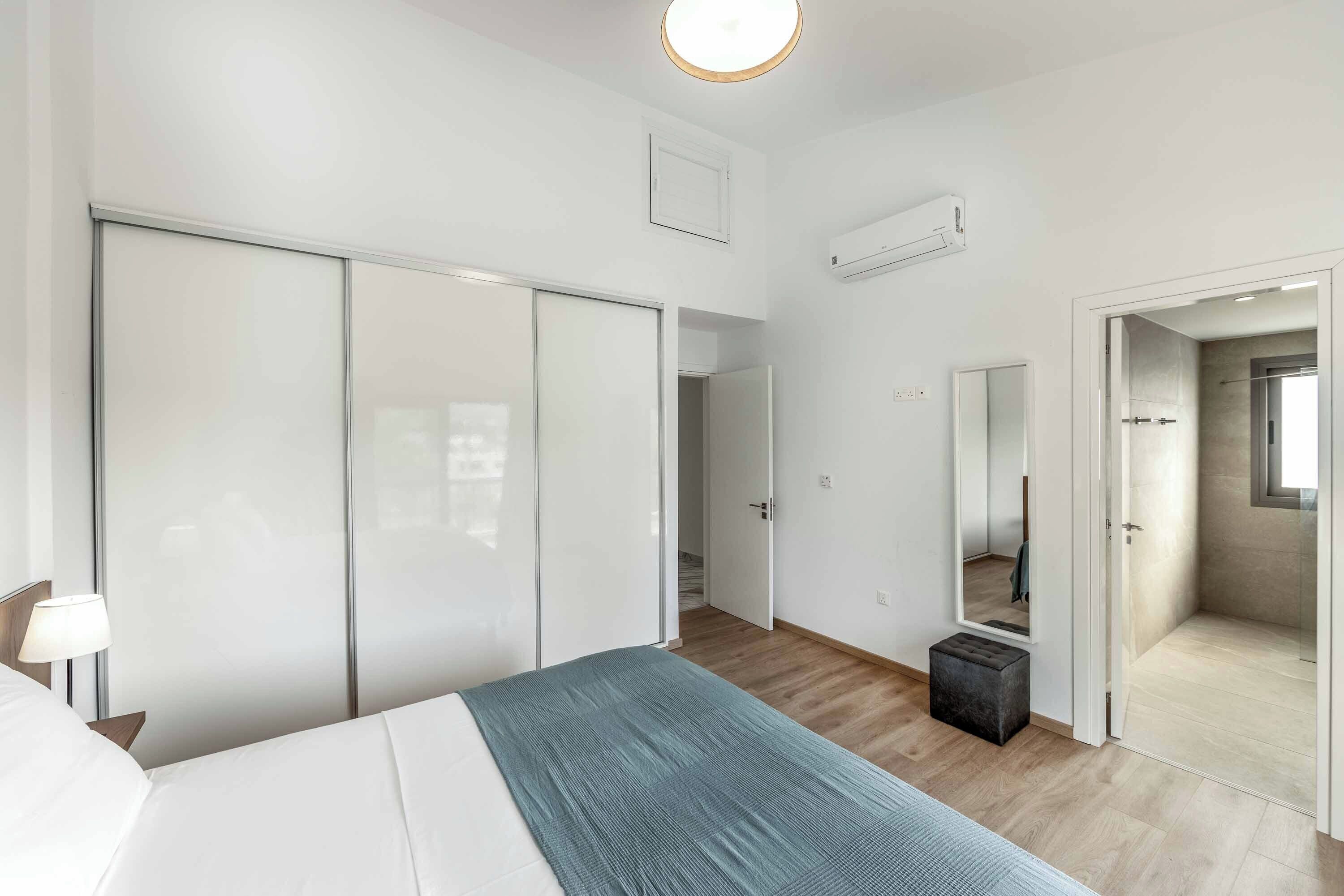Una habitación de hotel moderna con una cama grande, un armario, un espejo y un taburete pequeño.