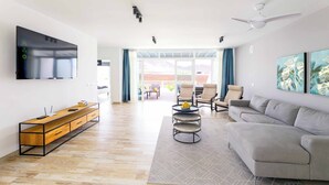 A spacious living room with a grey sofa, a wooden TV stand, and a flat-screen TV mounted on the wall. - Villa Bella (Yaiza)