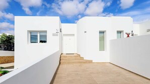 A modern, white-walled building with a tiled floor, a staircase leading to a door, and a small window on the left. - Villa Bella (Yaiza)