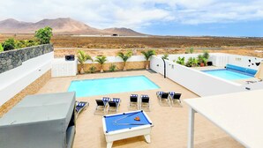 A pool area with a pool table, lounge chairs, and a view of mountains. - Villa Bella (Yaiza)