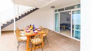 A dining area with a wooden table and wicker chairs, a staircase, and a sliding glass door leading to a balcony. - Villa Bella (Yaiza)