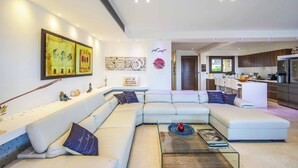A modern living room with a sectional sofa, a glass coffee table, and artwork on the walls. - Villa El Greco (Paralimni)