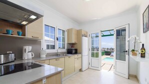 Cocina moderna con estufa integrada, cafetera y microondas. Se ve una piscina a través de los puertas de cristal.