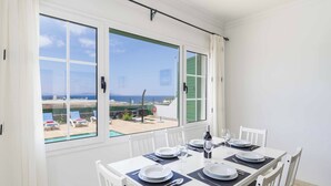 Un comedor con una mesa para cuatro, ventanas amplias con vista al mar y un balcón con piscina y sillas de descanso.