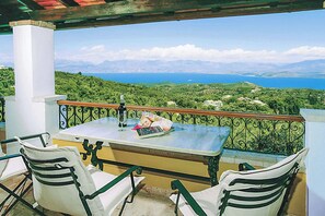 A balcony with a table and chairs, overlooking a scenic landscape with mountains and a body of water. - Villa Avgusta (Corfu)