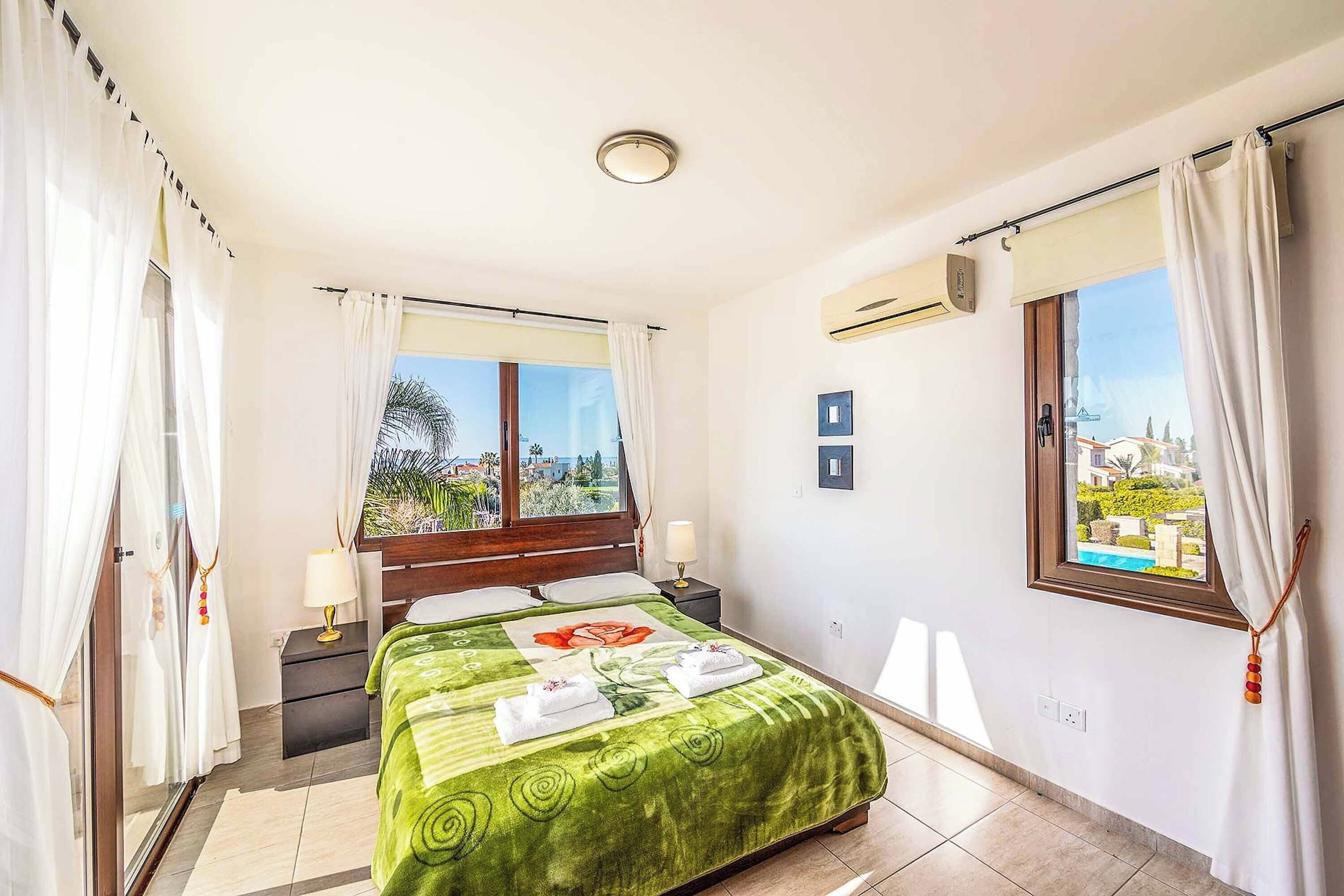A hotel room with a bed, two windows, a nightstand, and a view of a cityscape.