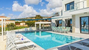 A modern outdoor swimming pool with lounge chairs and a view of the surrounding landscape. - Villa Alderbaran (Pegeia)