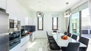 A modern kitchen with a dining area, large windows, and a view of the outside. - Villa Alderbaran (Pegeia)