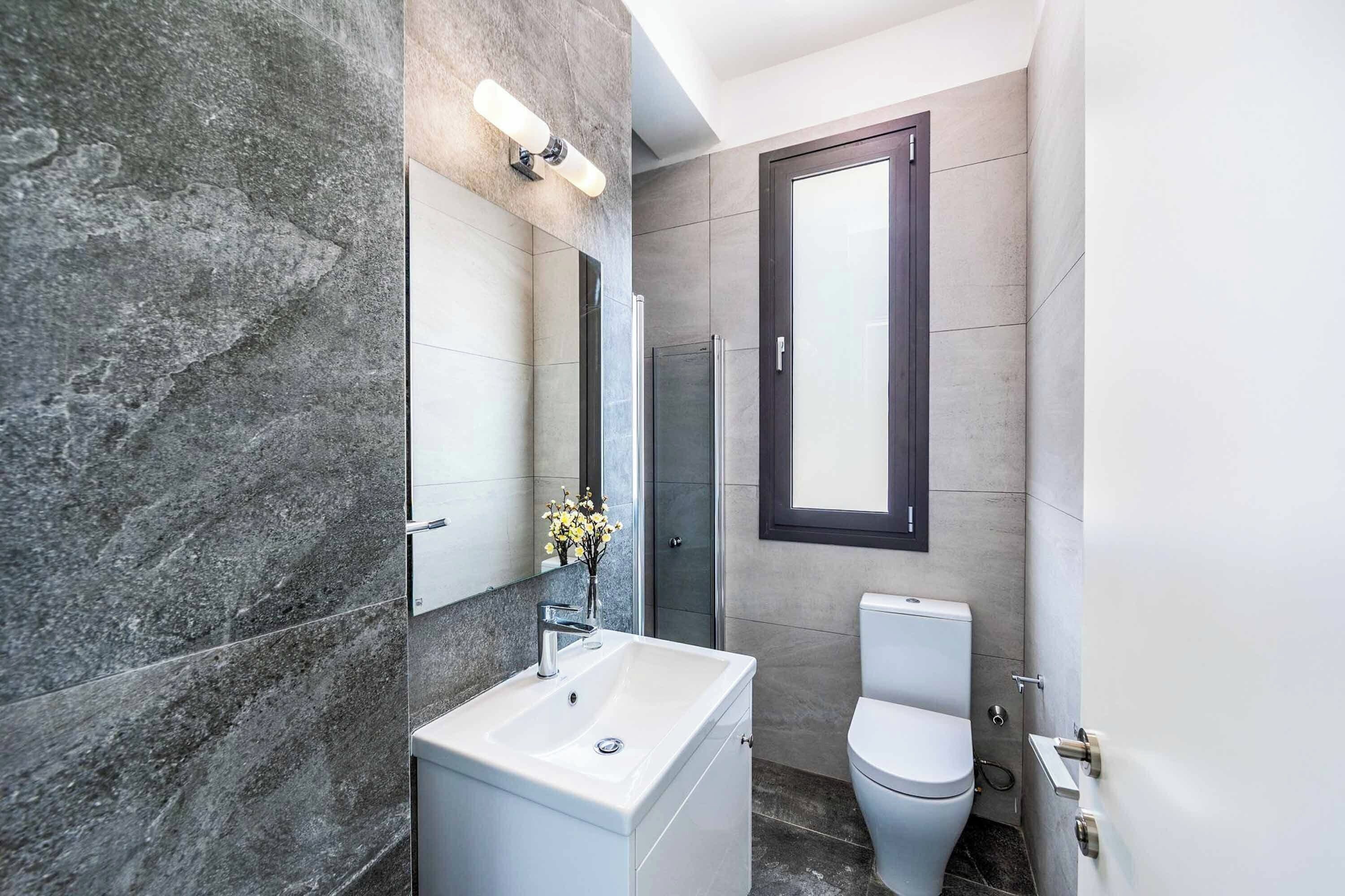 A modern bathroom with a marble sink, a glass shower enclosure, and a toilet.