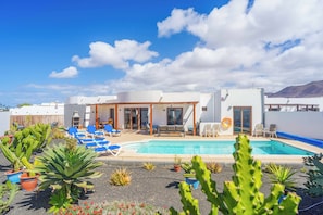 Un área de piscina con sillones de descanso, una piscina y cactus.