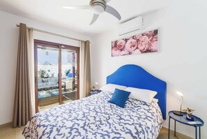 Un dormitorio con una cama grande, un ventilador de techo, una mesita de noche con lámpara y vistas a una piscina a través de una puerta corrediza.