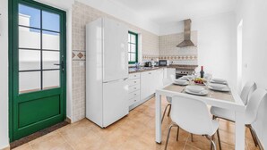 A compact kitchen with white cabinets, a green door, and a dining area with a white table and chairs. - Villa Bonaci (Yaiza)
