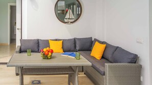 Una sala de estar moderna con un sofá seccional gris, un espejo redondo y una mesa con frutas y un libro.