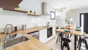 Una cocina moderna con un lavamanos de acero inoxidable, encimera de madera y una zona de comedor con taburetes.