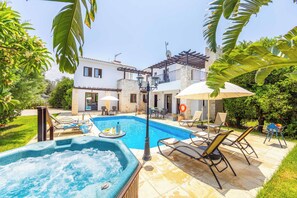 A swimming pool with lounge chairs and a hot tub, surrounded by a garden and a building with a balcony. - Villa Ay Kyriaki (Polis)