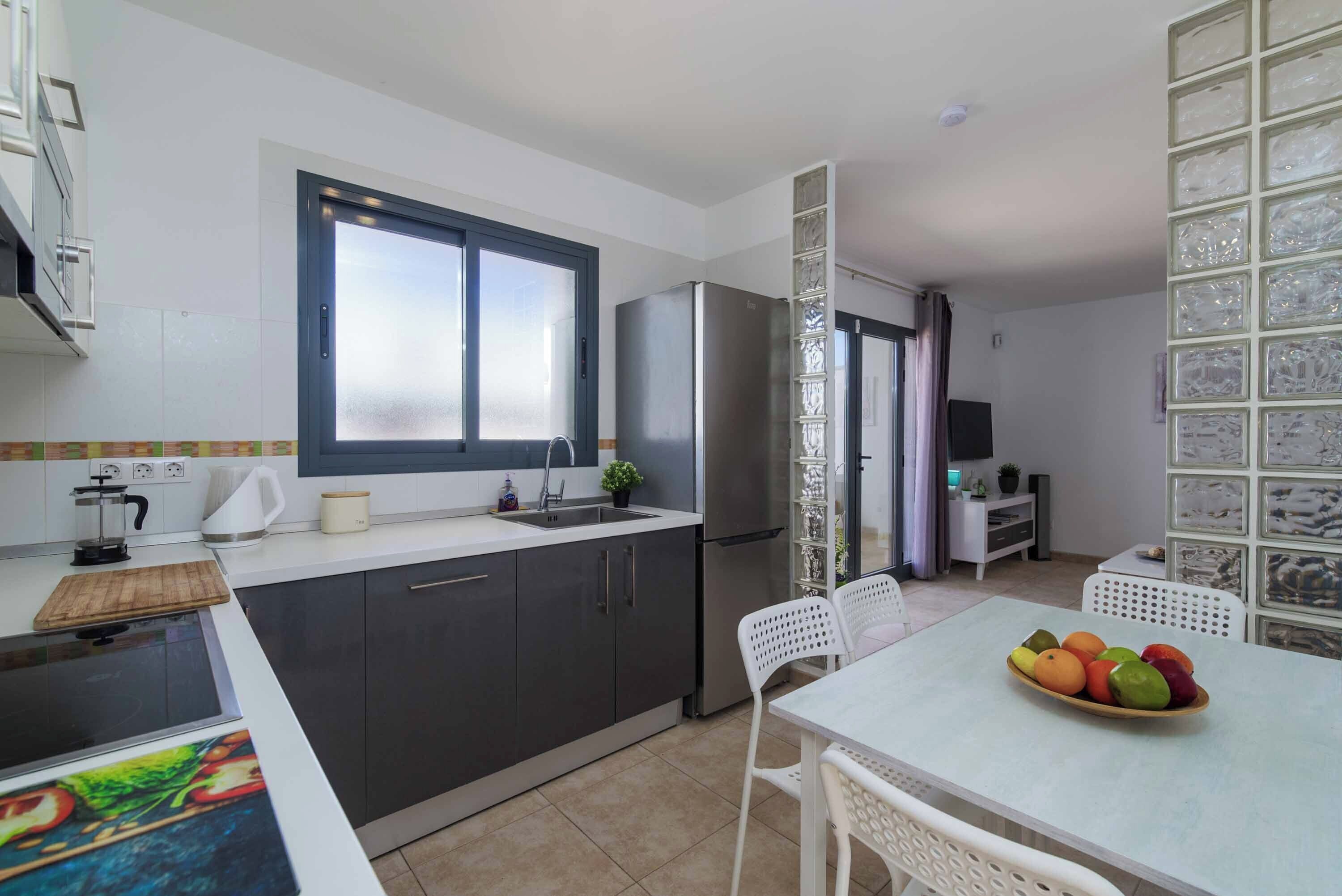 A modern kitchen with a built-in stove, a refrigerator, and a dining area with a table and chairs.