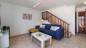 A living room with a blue sofa, a white coffee table, a staircase with wooden railings, and a door. - Villa Mia (Yaiza)