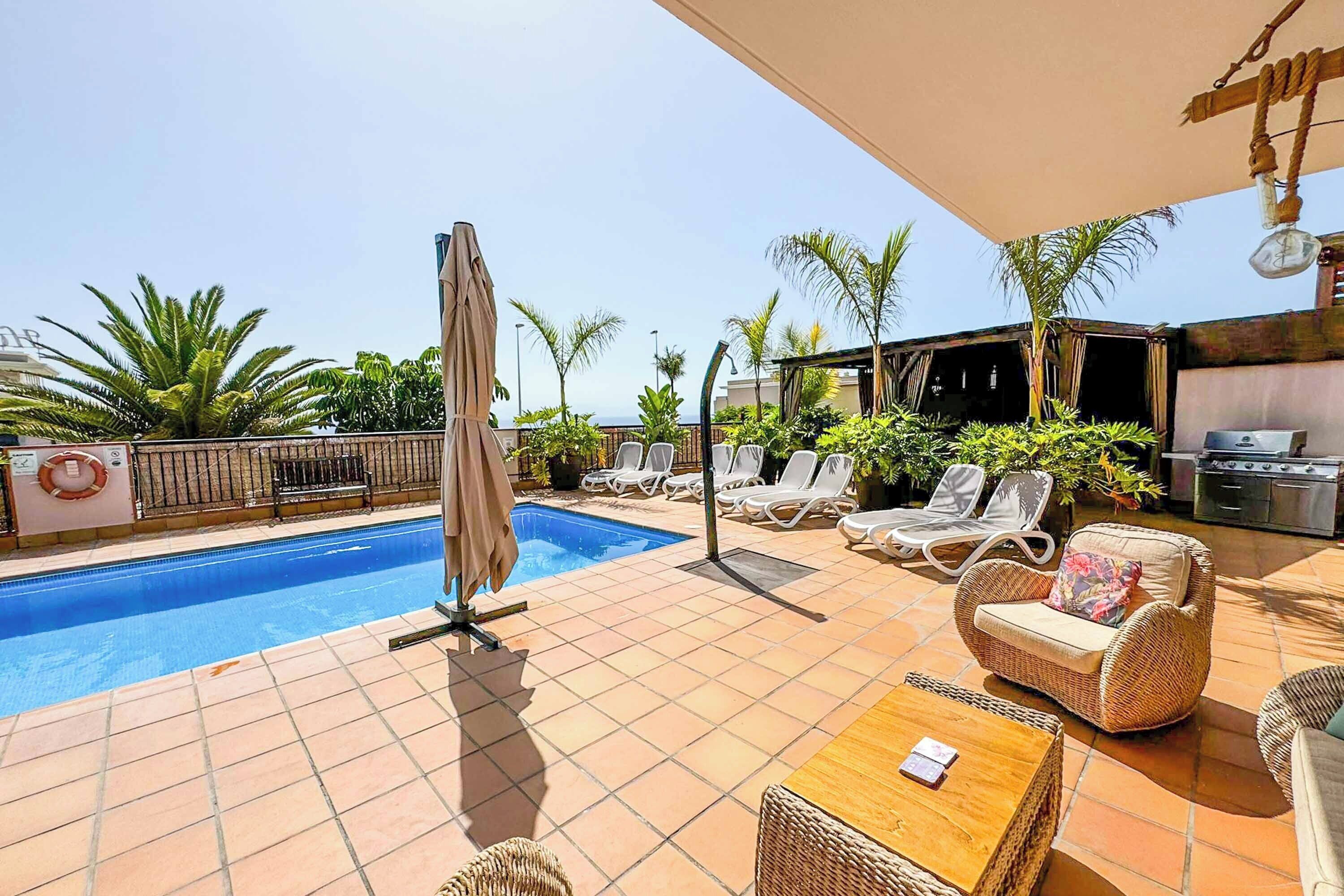 A poolside area with a swimming pool, lounge chairs, and a covered seating area.