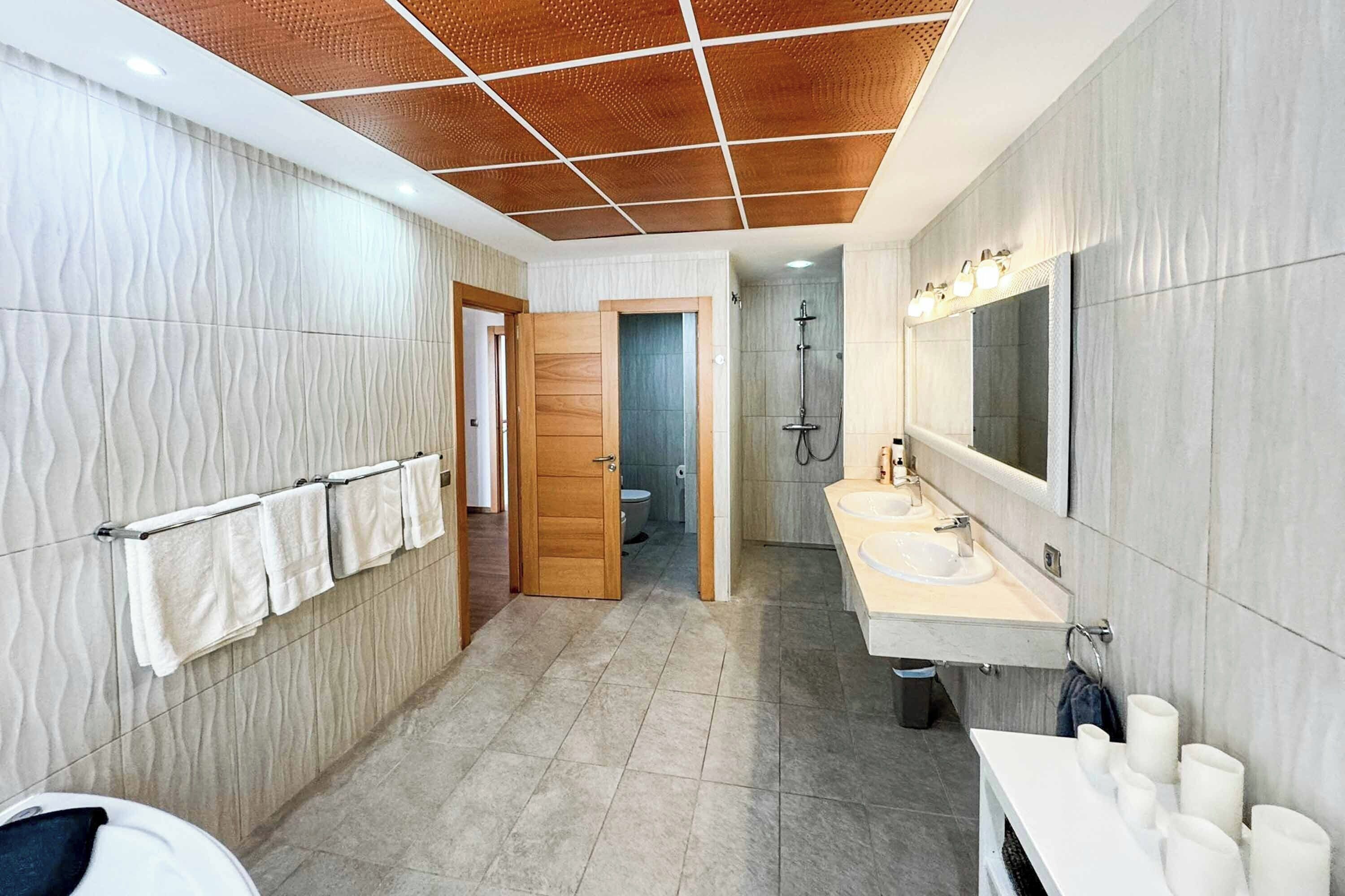 Een moderne badkamer met een houten deur, een douchegedeelte en een wastafel met een grote spiegel.
