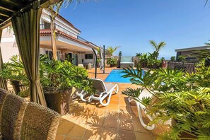 A poolside area with lounge chairs, potted plants, and a clear blue sky. - Villa Blossom (Santiago del Teide)