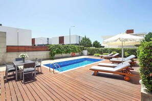 A rooftop pool area with a wooden deck, lounge chairs, and a table with chairs. - Villa Periwinkle (Paphos)