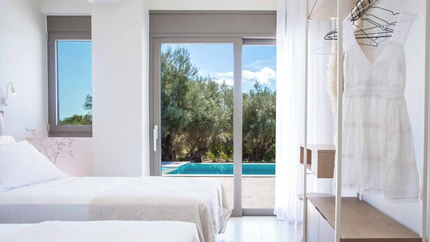 A bedroom with two beds, a view of a swimming pool, and a balcony with a view of trees. - Villa Averto Irene (Lefkada)
