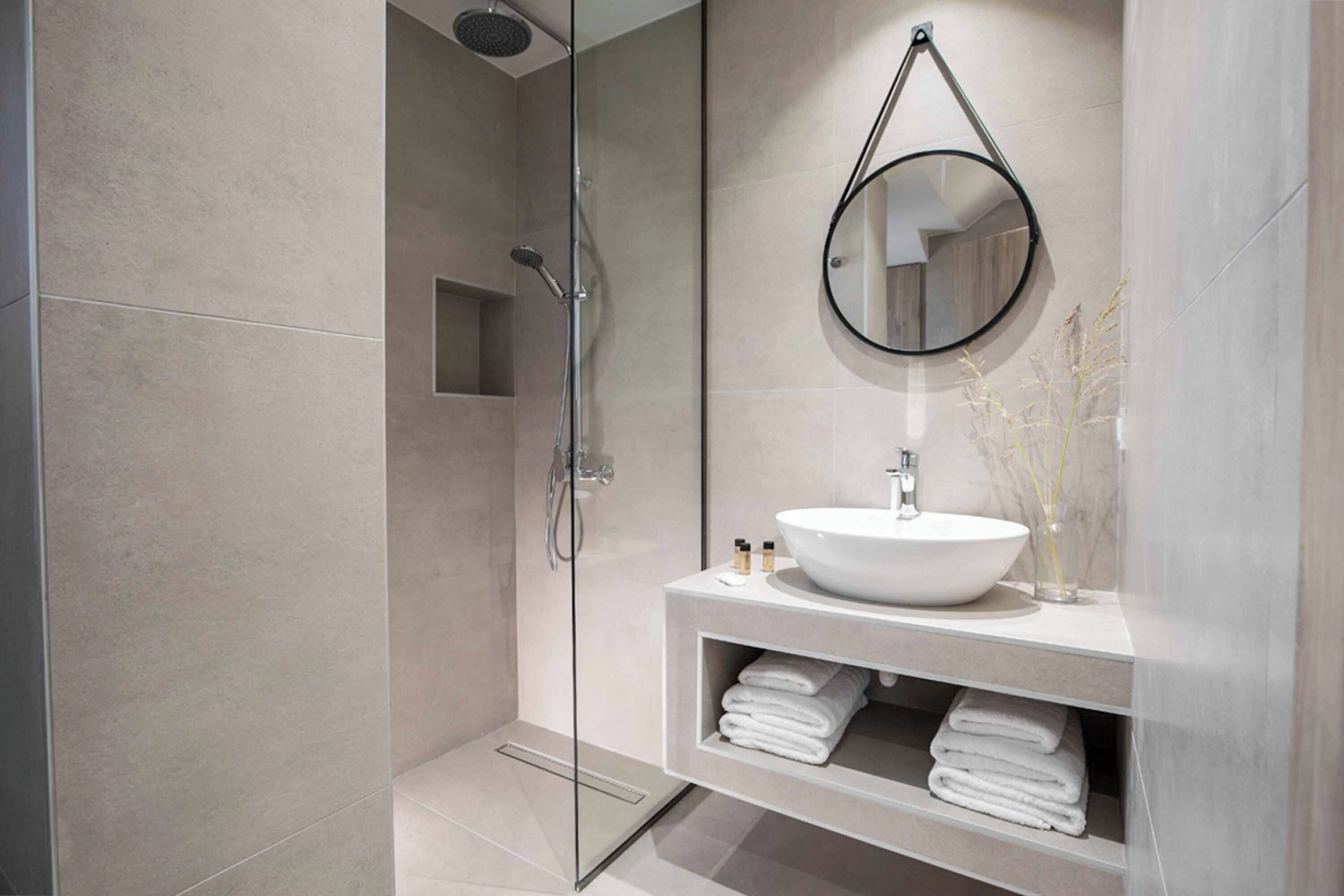 Une salle de bain moderne avec une douche à parois de verre, un lavabo blanc et un miroir rond.