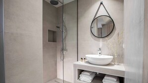 A modern bathroom with a glass-enclosed shower, a white sink, and a round mirror. - Villa Averto Irene (Lefkada)