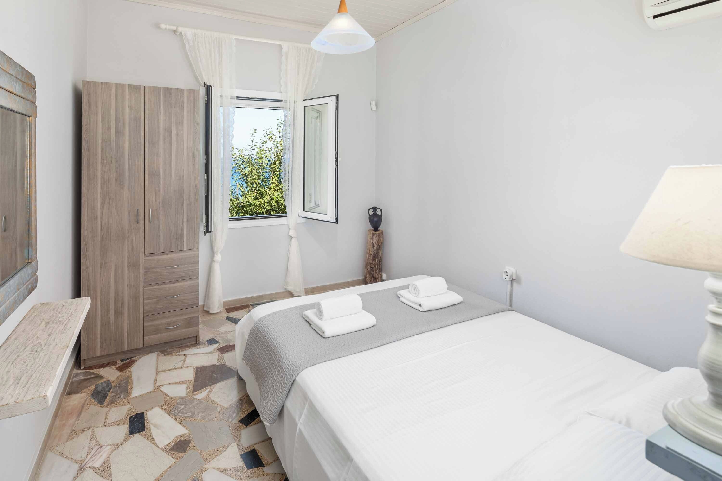 A hotel room with a bed, a nightstand, a lamp, a window with curtains, and a wardrobe.