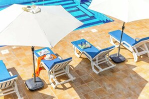 Un espace aménagé au bord de la piscine, avec des chaises longues, des parasols et une table sur laquelle se trouve un plateau avec divers objets.