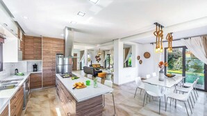 Cozinha moderna com ilha central, eletrodomésticos de aço inoxidável e área de jantar com mesa de vidro e cadeiras brancas.
