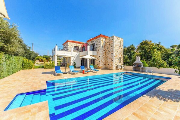 Une piscine aux carreaux bleus, un bâtiment en pierre avec un toit rouge et un balcon avec des chaises bleues.