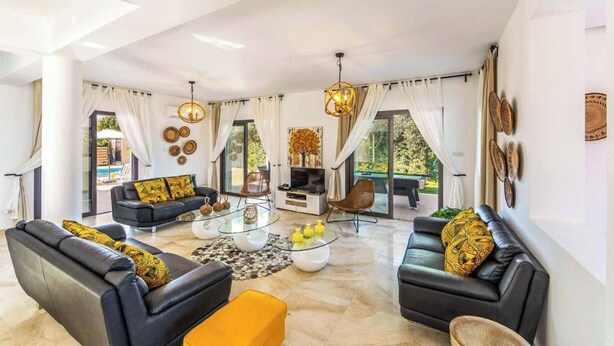 Uma sala de estar espaçosa com sofás de couro preto, uma mesa de centro de vidro e uma janela grande com cortinas.