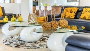 Uma sala de estar moderna com uma mesa de centro de vidro, um tapete estampado e um sofá com almofadas amarelas.