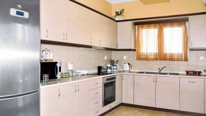 A modern kitchen with stainless steel appliances, beige cabinetry, and a window with sheer curtains. - Villa Carreta (Corfu)