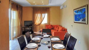 A dining area with a table set for six, a sofa, and a television in the background. - Villa Carreta (Corfu)