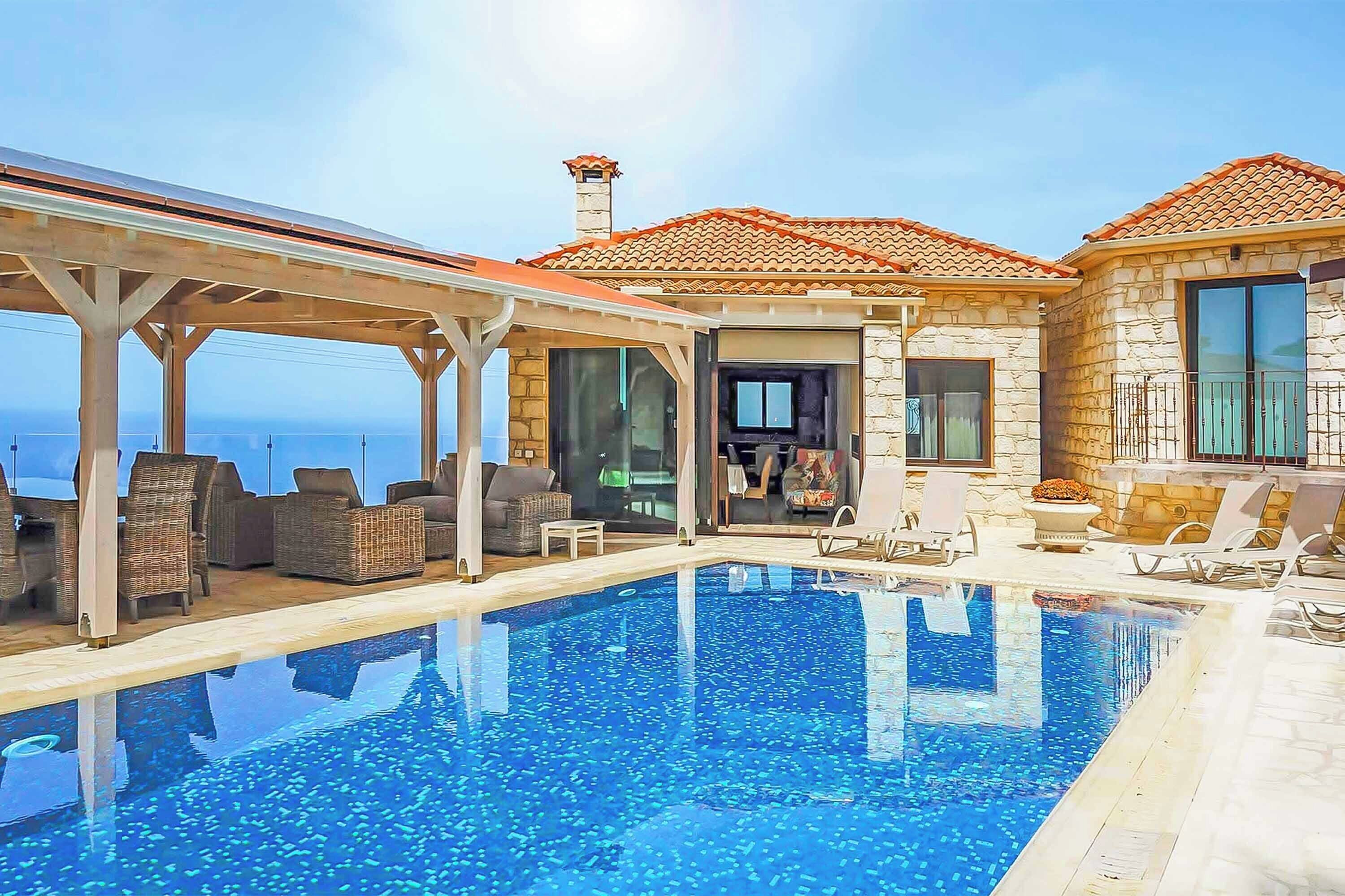 A pool area with a clear view of the sea, stone walls, and outdoor seating.