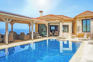 A pool area with a clear view of the sea, stone walls, and outdoor seating.